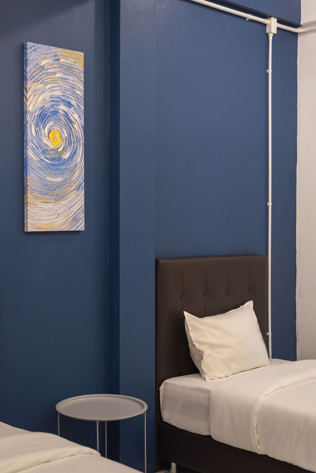 A bedroom with a single bed, a bedside table, and a wall-mounted painting.