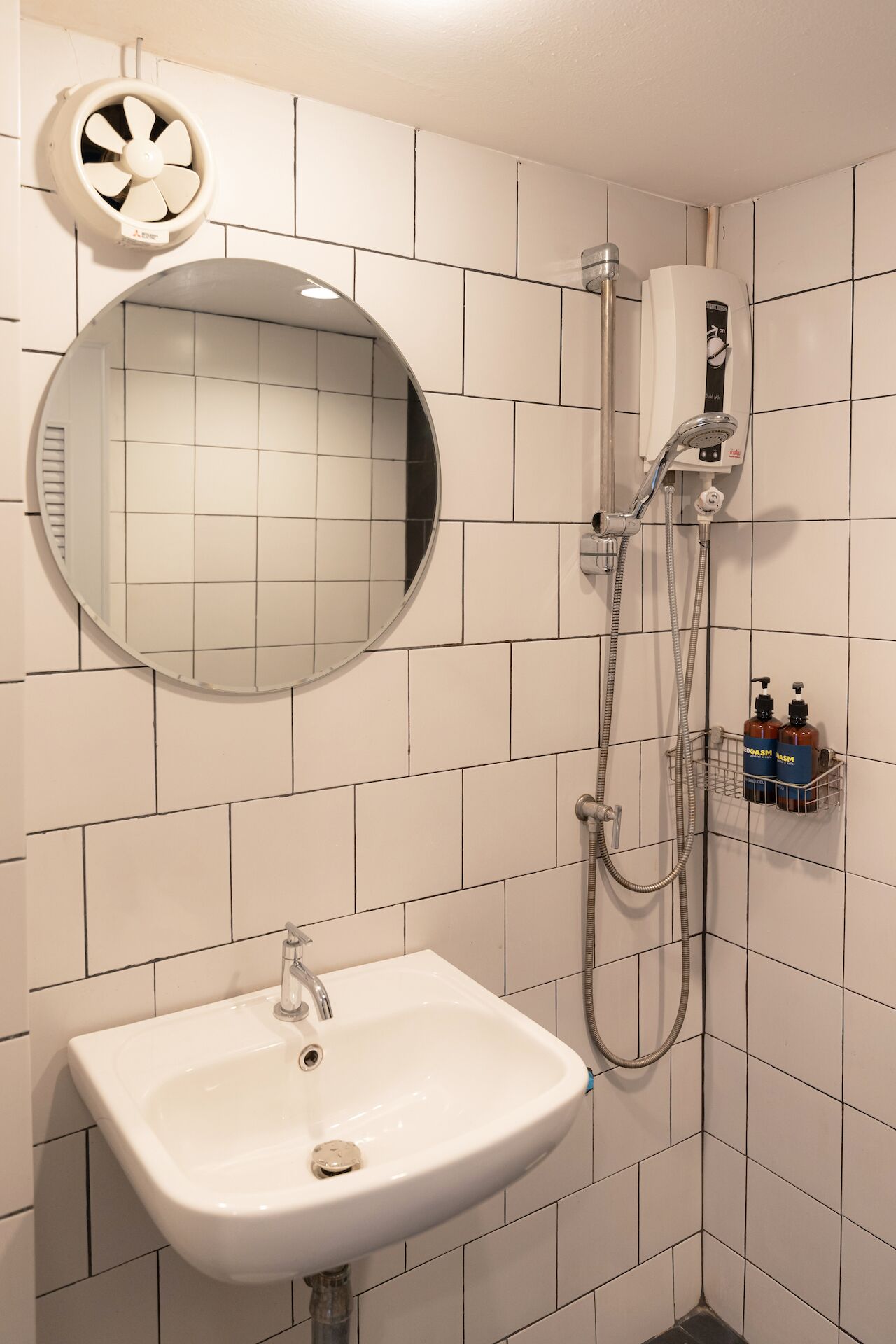 Un baño con un lavabo blanco, un espejo redondo, un cabezal de ducha manual y un calentador de pared.