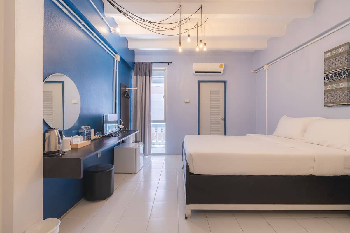 A modern bedroom with a bed, a desk with a computer, a mirror, and an air conditioning unit.