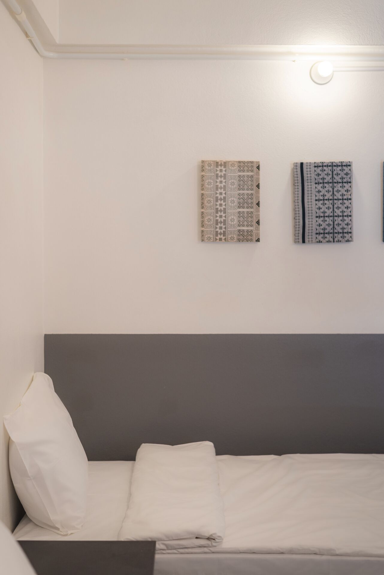 A neatly made bed with white linens, a gray headboard, and two patterned wall decorations.