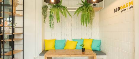 A cozy seating area with a wooden table and bench, two hanging plants, and a wall-mounted shelf with decorative items.