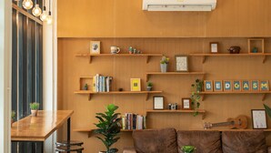 A cozy living area with a wooden sofa, a coffee table, and a bar area with stools. Shelves with books and decorative items are visible. - BEDGASM Hotel x Café at Nimman (Chiang Mai)