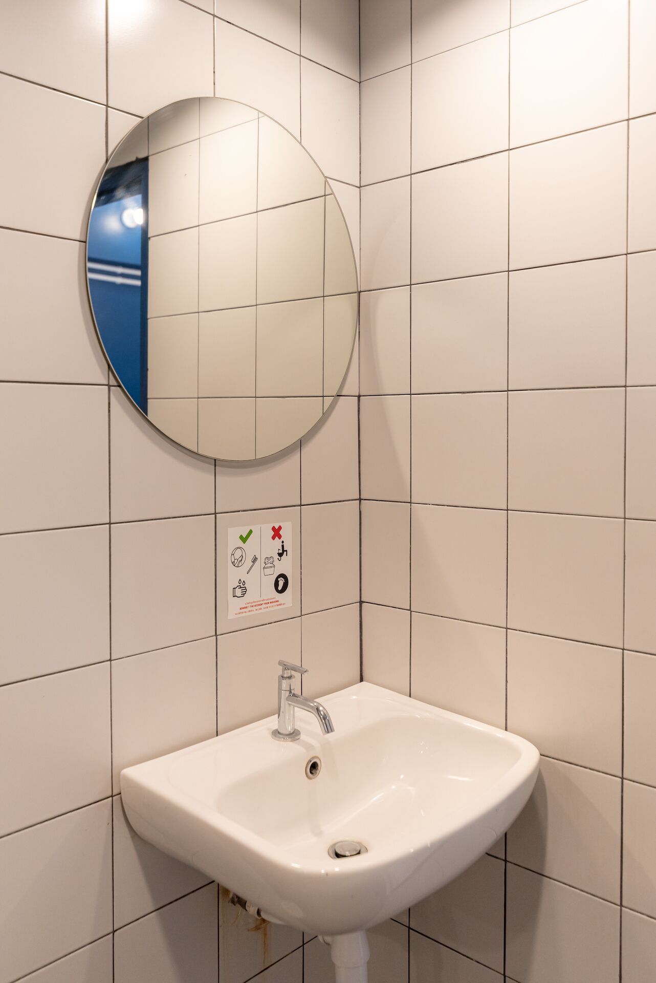 A bathroom with white tiles, a round mirror, and a sink with a faucet.