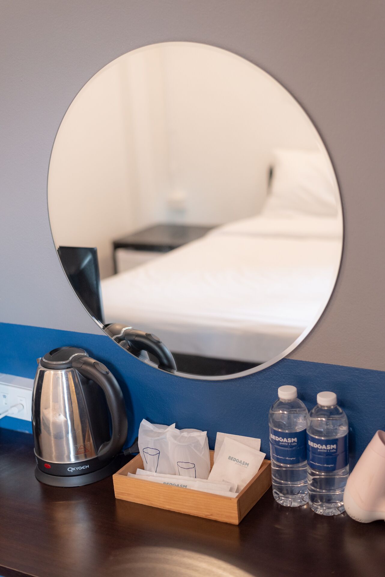 Une chambre d’hôtel comprenant un lit, une table de chevet avec une bouilloire, un miroir et un plateau avec des bouteilles d’eau et des mouchoirs.