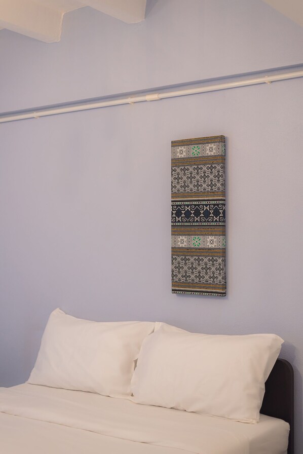 A bed with white bedding in a room with a light blue wall and a patterned tapestry hanging above it.