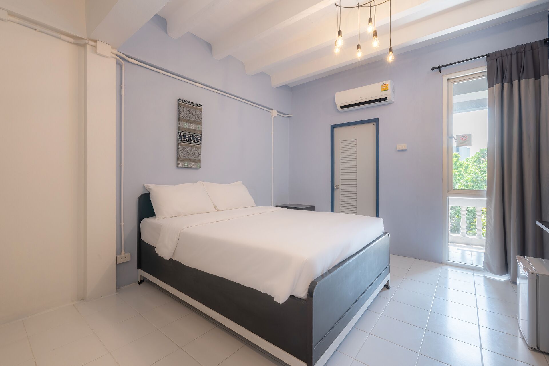 Un dormitorio con cama, mesita de noche, equipo de aire acondicionado, una puerta y vistas al exterior.
