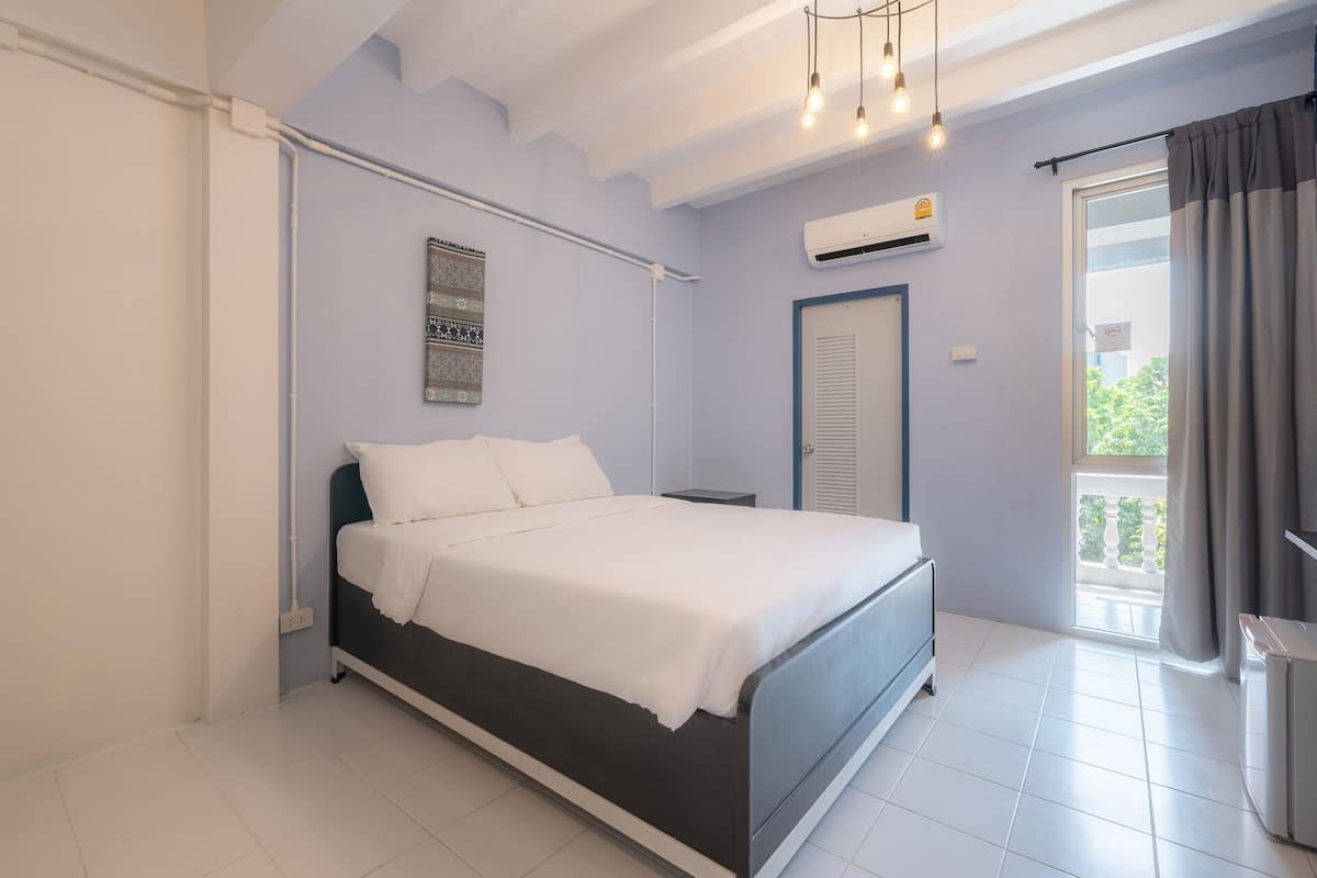 A bedroom with a bed, a nightstand, an air conditioning unit, a door, and a view of the outside.