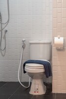 A white toilet with a blue towel, a shower hose, and a toilet paper holder on a white tiled wall.