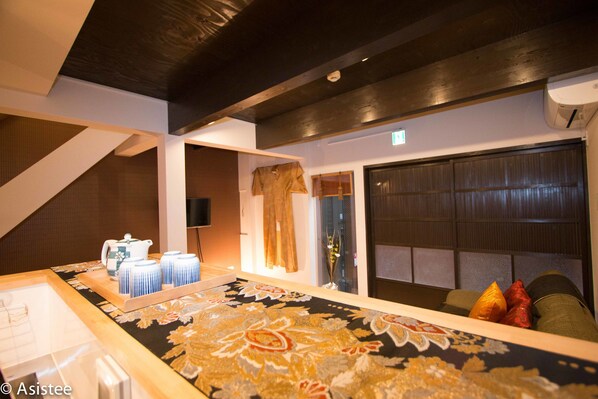 Quarto de hotel com uma cama grande, uma mesa pequena com uma bandeja de chá e um bule, uma janela com cortinas e vista para o exterior.