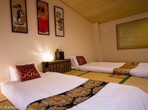 Quarto de hotel com duas camas, uma mesinha com abajur e três quadros decorativos na parede.