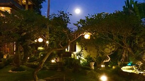 Un jardin avec un sentier, des arbres et un bâtiment, et on peut voir la lune dans le ciel.