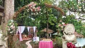 Une cérémonie de mariage organisée dans un jardin, avec un chemin en pierre, des décorations florales et une statue.
