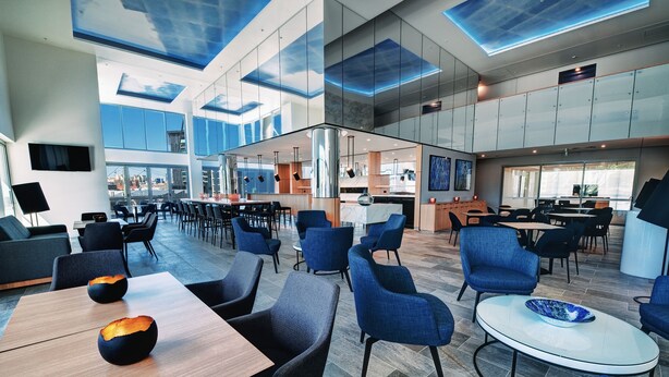 Un moderno vestíbulo de hotel con un diseño espacioso, una zona de bar central y grandes ventanales que ofrecen vistas a la ciudad.