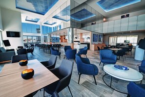 A modern hotel lobby with a spacious layout, a central bar area, and large windows offering views of the city. - Belise Apartments (Bowen Hills)