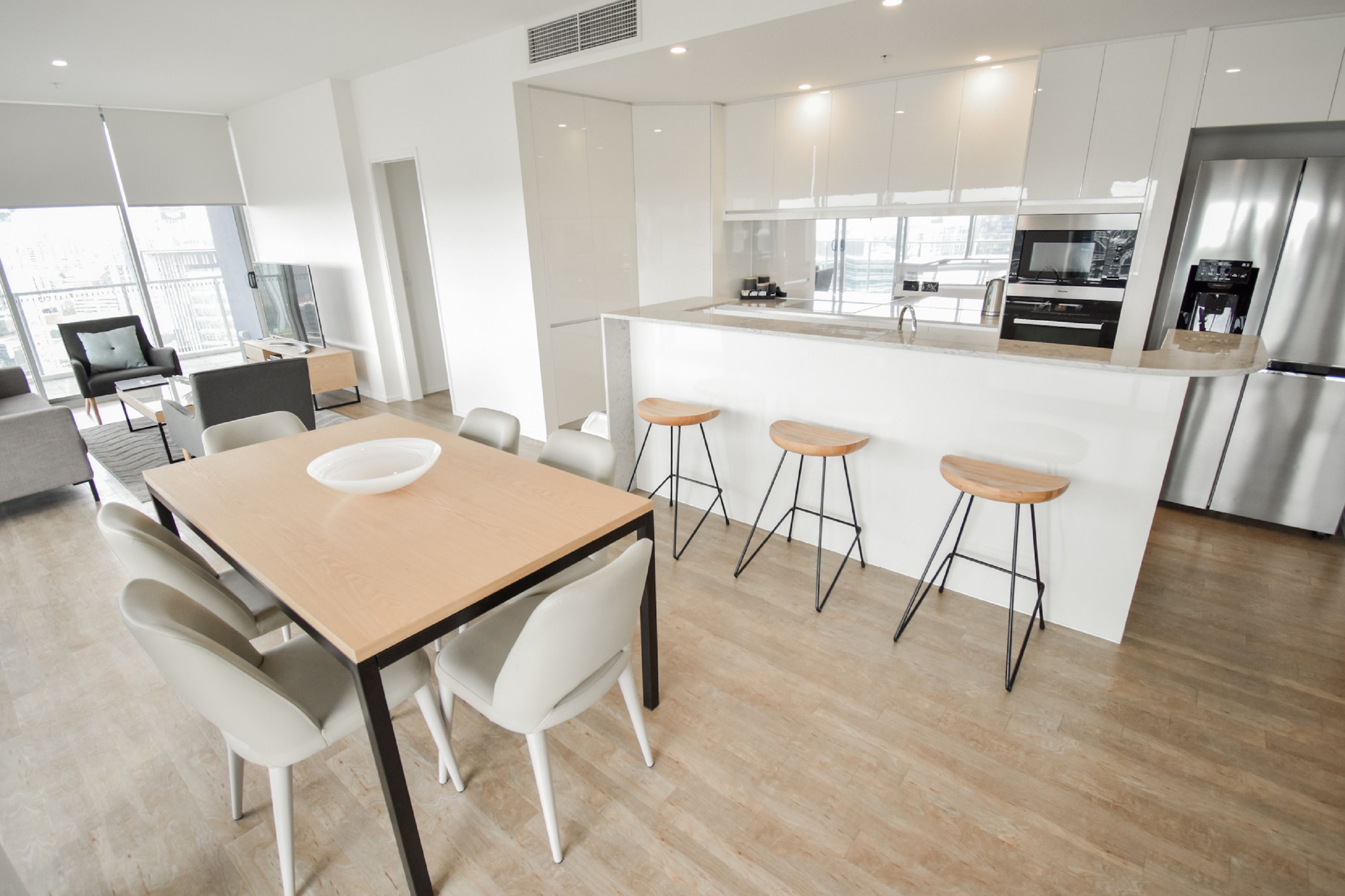 Una cocina moderna con una isla central, taburetes de bar y una zona de comedor con mesa y sillas.
