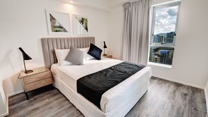 Una habitación de hotel moderna con una cama grande, dos mesitas de noche, una ventana con cortinas y una obra de arte en la pared.