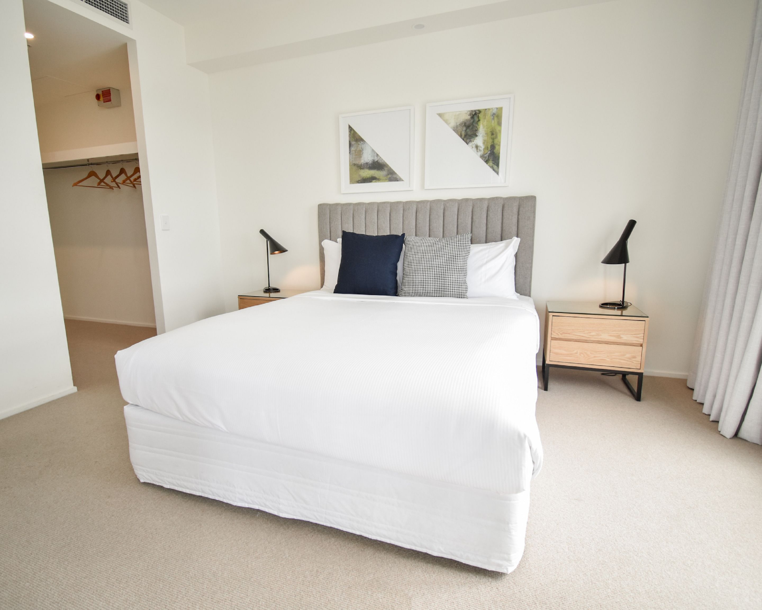 A hotel room with a large bed, two bedside tables with lamps, a grey upholstered headboard, and two framed pictures on the wall.