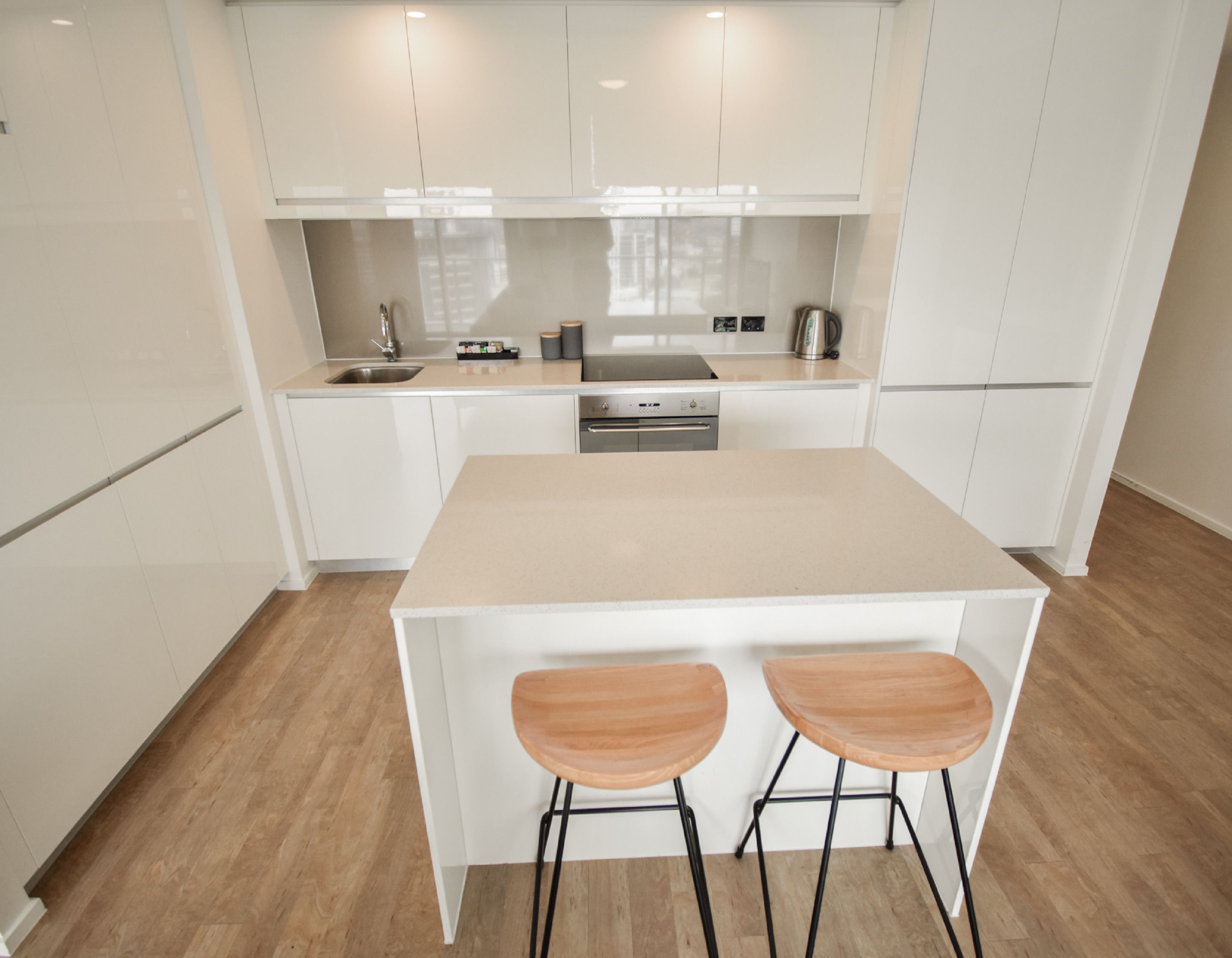 A modern kitchen with white cabinets, a central island with stools, stainless steel appliances, and a wooden floor.