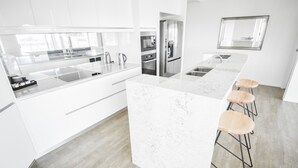 Una cocina moderna con armarios blancos, una isla de mármol y taburetes de madera.