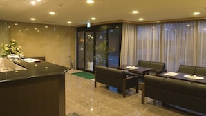 A hotel lobby with a reception desk, seating area, and large windows with curtains. - Aoi Hotel (Nagoya)