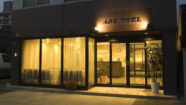 A hotel entrance with a reception desk, glass doors, and potted plants. - Aoi Hotel (Nagoya)