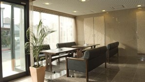 A hotel lobby with a large potted plant, seating area with tables and chairs, and a large wardrobe. - Aoi Hotel (Nagoya)