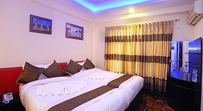 A hotel room with a large bed, two framed pictures on the wall, a bedside table with a phone, and a minibar. - Hotel Gallery Nepal (Kathmandu)