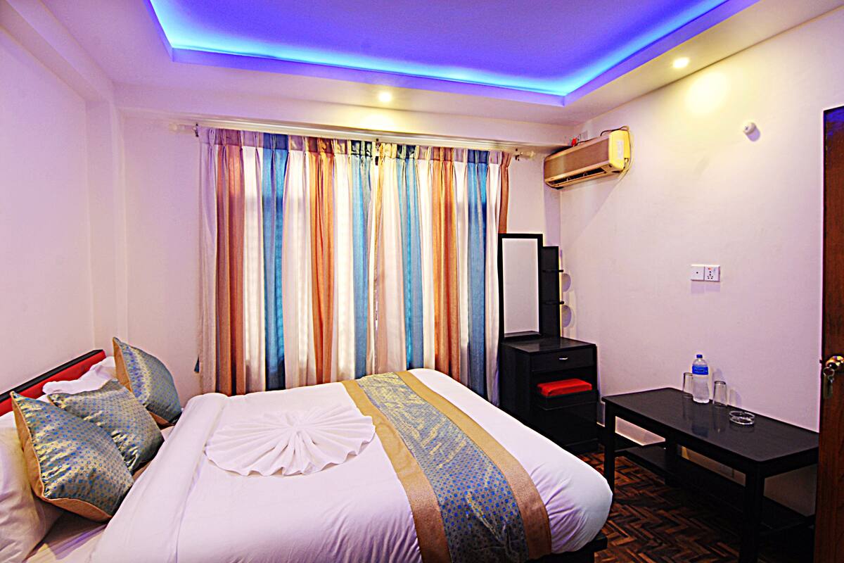 Una habitación de hotel con cama, escritorio, espejo y ventana con cortinas.