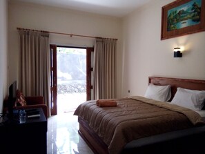 A hotel room with a bed, a desk with a computer and a bottle, and a painting on the wall. - Family Garden Homestay (Senggigi)
