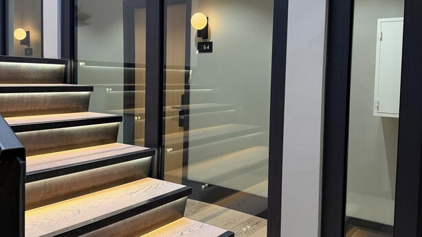 Una escalera moderna con peldaños de madera y puertas de vidrio que dan a una habitación.