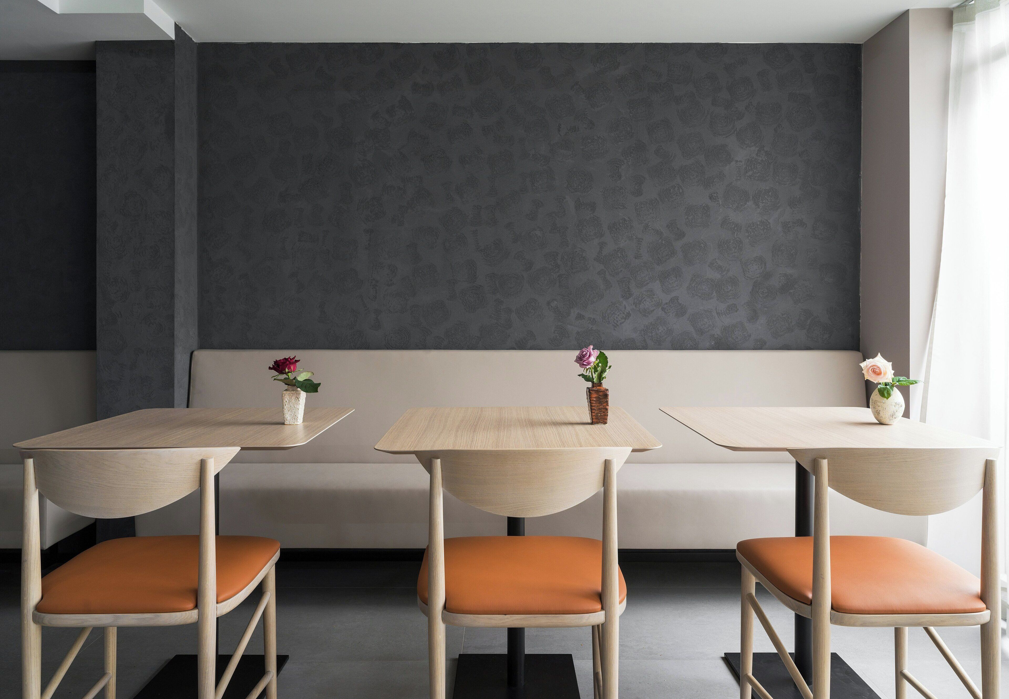 A modern interior with three wooden tables and matching chairs, a grey patterned wall, and a bench.