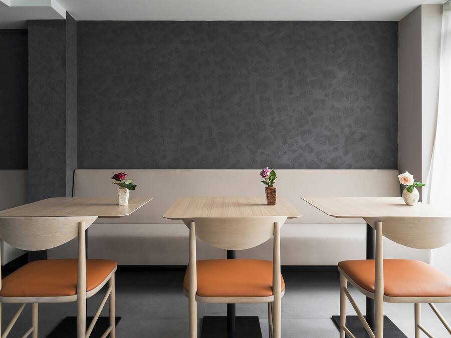 A modern interior with three wooden tables and matching chairs, a grey patterned wall, and a bench.
