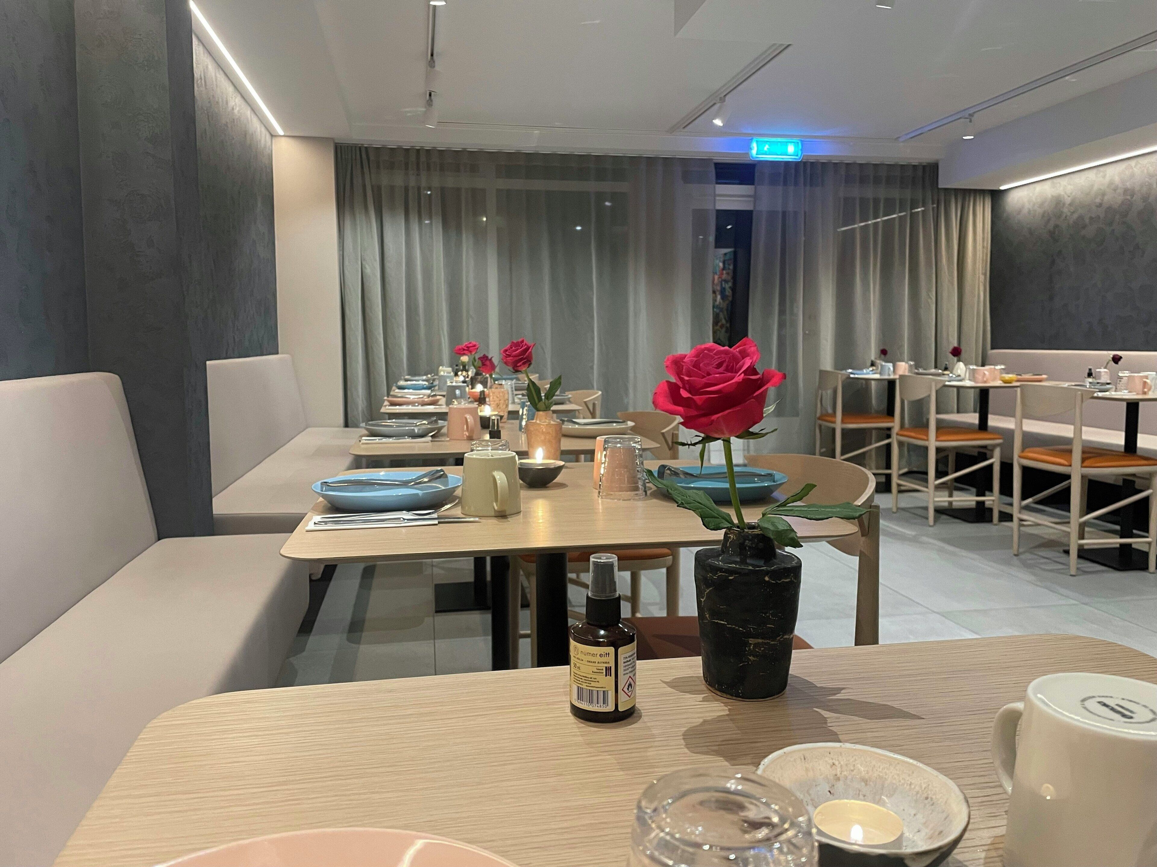 A dining area with tables set for two, featuring modern decor and a vase with a single red rose.
