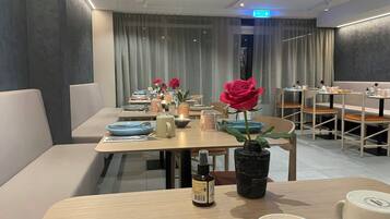 A dining area with tables set for two, featuring modern decor and a vase with a single red rose.