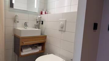 Un baño moderno con lavamanos, espejo e inodoro blancos.