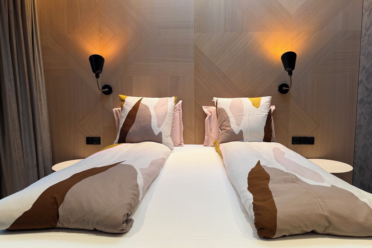 A modern hotel room with a large bed, two wall-mounted lamps, and a wooden textured wall.