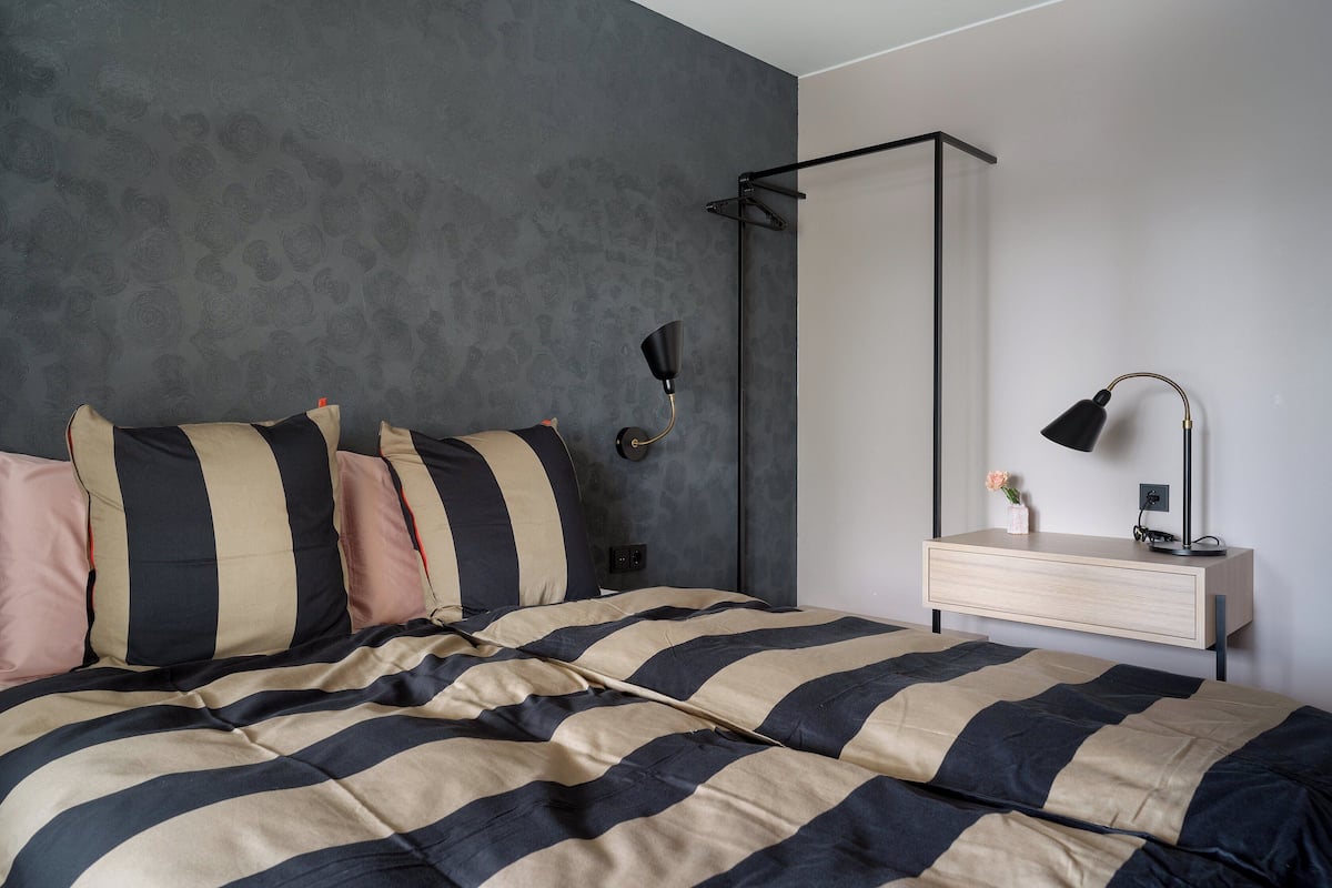 A bedroom with a bed, a bedside table, a lamp, and a wall-mounted shelf.