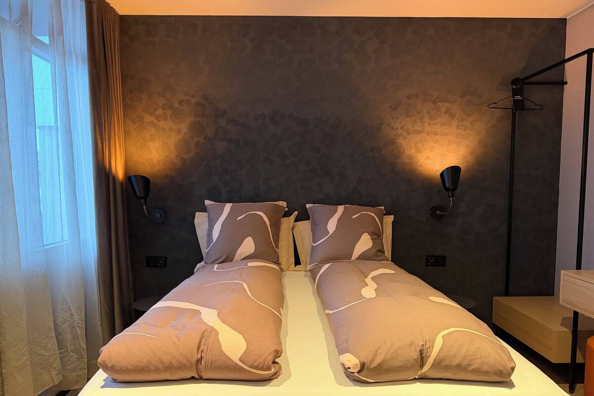 A double bed with patterned pillows, a bedside table, and wall-mounted lamps.