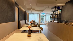 Un restaurante moderno con mesas de superficie de mármol, una zona de bar con estanterías y vistas al exterior a través de amplias ventanas.