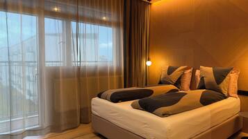 A hotel room with a large bed, sheer curtains, a wooden floor, and a nightlight.