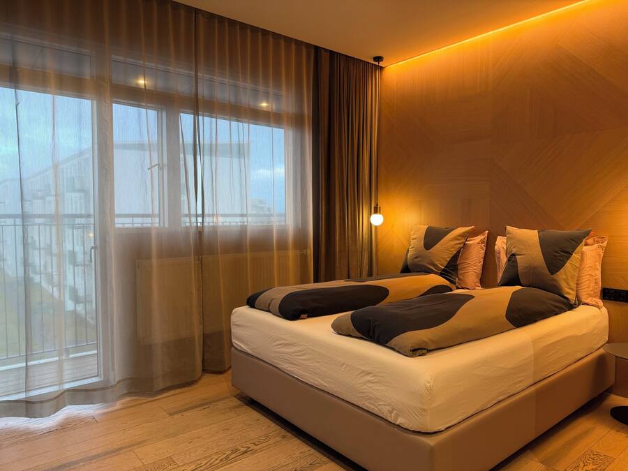 A hotel room with a large bed, sheer curtains, a wooden floor, and a nightlight.