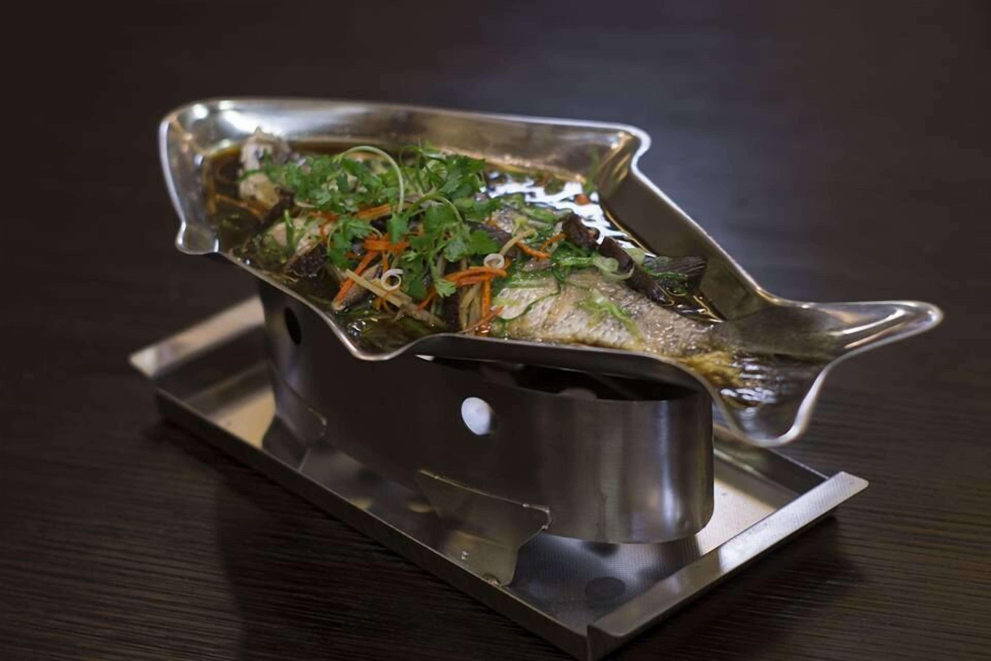 Un plato de pescado servido en un recipiente metálico con forma de barco.