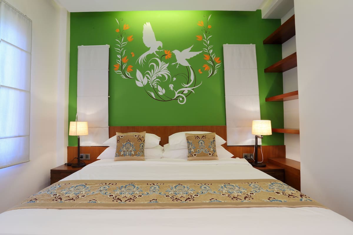 A hotel room with a green accent wall, a bed with white linens, two bedside lamps, and a decorative headboard.