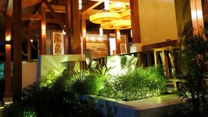 A well-lit indoor space with wooden beams, hanging lamps, and a planter with green plants. - Mount Inle Hotel & Resorts (Nyaungshwe)