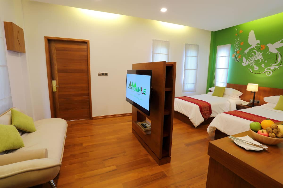 A hotel room with two beds, a TV, a wooden desk, and a fruit bowl.