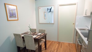 A dining area with a wooden table and chairs, a framed picture on the wall, and a kitchen with a sink and cabinets. - Westside Studio Apartments (Armidale)