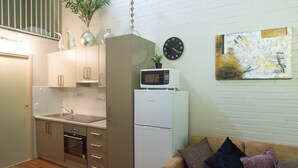 A compact kitchen with a microwave, refrigerator, and a sink. There's a small dining table and a sofa with cushions. - Westside Studio Apartments (Armidale)