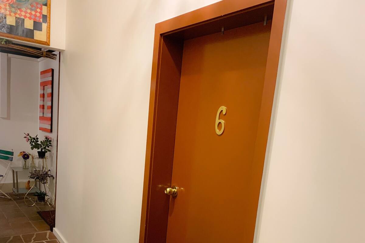 A wooden door with the number 6, a stone-tiled floor, and a wall with a framed picture.