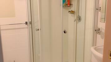 A modern bathroom with a glass-enclosed shower, white tiles, a glass shower door, a towel rack, a toilet, and a sink.