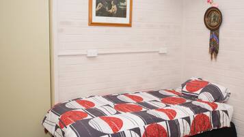 Una habitación pequeña con cama individual, pared de ladrillo blanco, un cuadro enmarcado y un adorno colgante.